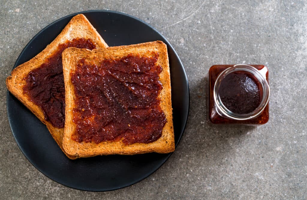 Тосты с мармайтом (Marmite) на чёрной тарелке, вид сверху, и баночка пасты